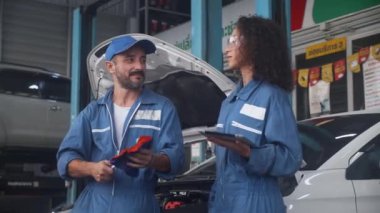 Tamirci ekibi, elinde üniformalı bir kadın ve erkek bilgisayarla garajda araba incelemesi, oto servis, teşhis ve kontrol aracı teknisyeni hakkında konuşuyor ve tartışıyorlar..