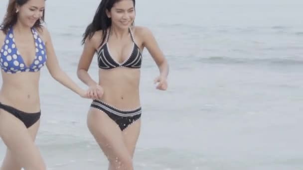 美しい二人の若いアジアの女性ビキニビーチで実行しています レジャーのための休暇で夏の旅行で幸せな女の子セクシー 女性は 熱帯で海の上に水着や水着を身に着けてリラックス スローモーション — ストック動画