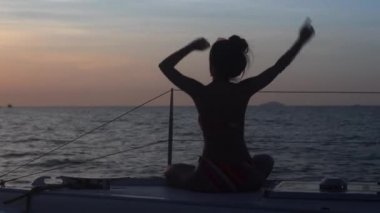 Mutlu siluet güzel Asyalı kadın seksi bikinili dans ediyor ve yaz tatilinde birlikte yelkenli gezintisinde eğleniyorlar. Akşamları gün batımında tekne gezisinde kız kıza eğleniyorlar..