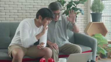 Mutlu baba ve oğul kanepede oturup aileleri ile birlikte evdeki oturma odasındaki dizüstü bilgisayarlarda, yaşlılar ve gençler video konferansında ilişki, iletişim konseptiyle sohbet ediyorlar..