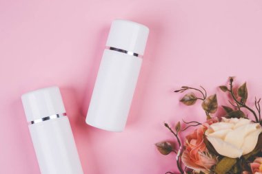 Pembe arka planda izole edilmiş krem ya da losyonlu makyaj şişesi ve çiçek, reklam, cilt bakımı ya da kozmetik, üst görünüm, düz döşeme, cilt bakımı ve ürün ile tedavi paketi.