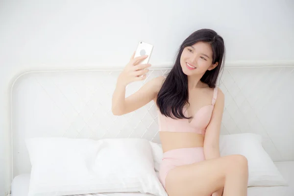 美しいです若いですアジアの女性セクシーで下着話上の自撮りスマートフォン上のソーシャルネットワークのためにザベッドルーム 女の子でランジェリーリラックスで写真を撮るとともに携帯電話でベッドルーム — ストック写真