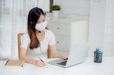 İnternette kulaklık takan genç Asyalı bir kadın. Masasında e-öğrenme, kulaklık takan bir kız. Evde dizüstü bilgisayarla interneti öğrenen bir kız..