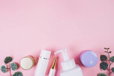 Pembe arka planda izole edilmiş krem ya da losyonlu makyaj şişesi ve yaprak, reklam, cilt bakımı ya da kozmetoloji, üst görünüm, düz döşeme, cilt bakımı ve ürün ile tedavi paketi.