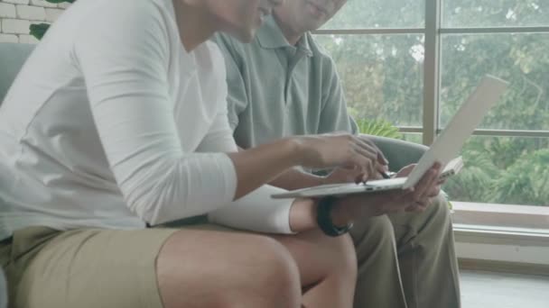 父亲坐在沙发上看笔记本电脑的家庭 以及与儿子在家 老人和年轻人上网购物 商业概念一起在笔记本上填写核对表的家庭 — 图库视频影像