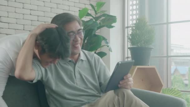 父と息子と幸せな家族がソファに座って 家でタブレットコンピュータに興味を持って話し合い 高齢者や若者がタブレットを見て話し合い コミュニケーションの概念 — ストック動画