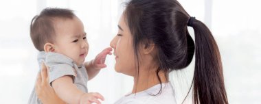 Genç Asyalı anne küçük bebeği yatak odasında birlikte tutuyor, anne çocuğu ve bakımı taşıyor, kadın ve çocuğu tasasız, yeni yürümeye başlayan çocuk, duygu ve ifade, aile kavramı.