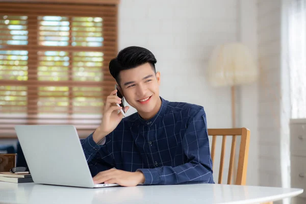 아시아인 남자가 전화를 노트북 컴퓨터를 가지고 집에서 일하고 노트북을 사용하여 — 스톡 사진