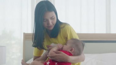 Genç Asyalı anne, küçük bebeği evde süt şişesiyle kucaklıyor ve besliyor. Yeni doğmuş masum bir anne, anne ve çocuğun ilişkisinden ve bağ kurmasından tatmin oluyor. Aile kavramı..