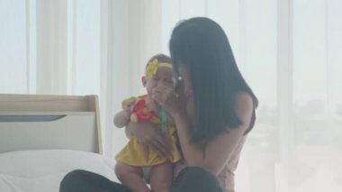 Genç Asyalı anne ve bebek yatakta birlikte oturup oynuyorlar, anne ve kız, duygu ve ifade ailesi mutlu, ebeveyn ve yeni doğmuş, rahatla ve pozitif, duygu ve ifade.