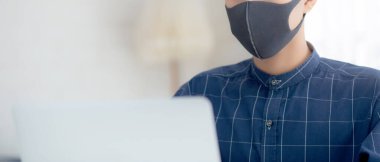 Maskeli genç bir iş adamı, masadaki dizüstü bilgisayarla covid-19 salgını ve sağlık hizmetleri için çalışıyor. Erkek karantina masasında defter kullanarak evde kalıyor..