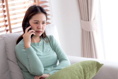 Asyalı genç bir kadın evdeki akıllı telefonuyla konuşurken koltukta oturmuş endişeli ve stresli bir şekilde oturuyor. Mutsuz ve endişeli bir kadın akıllı telefondan, yaşam tarzından ve iletişimden bahsediyor..
