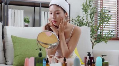 Evdeki oturma odasında kırışıklıkları kontrol etmek için aynaya bakan genç Asyalı güzel bir kadın, nemlendirici süren mutlu bir kadın. Hijyen, cilt bakımı, cilt bakımı, cilt bakımı ve cilt bakımı..