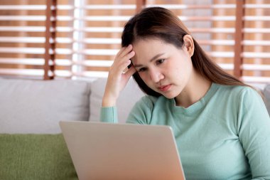 Genç Asyalı iş kadını evde stresli ve hayal kırıklığına uğramış bir şekilde dizüstü bilgisayarla çalışıyor, iş kadını defterinde üzgün ve yorgun olarak kullanıyor, ifade ve duygu, iş ve yaşam tarzı.