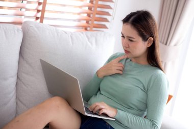 Genç Asyalı iş kadını laptopla çalışırken düşünceli bir şekilde ofisteki koltukta oturuyor, iş kadını evdeki not defterini kullanıyor, kadın dizüstü bilgisayarla düşünüyor..