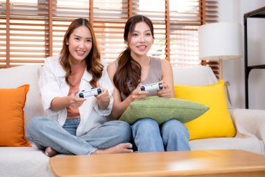 İki Asyalı kadın, evdeki rahat bir oturma odasında bilgisayar oyunu oynuyorlar. Eğlence, arkadaşlık ve neşeli bir yaşam tarzı. Asyalı arkadaşlar, eğlence ve oyun paylaşımının keyfini çıkarıyorlar..