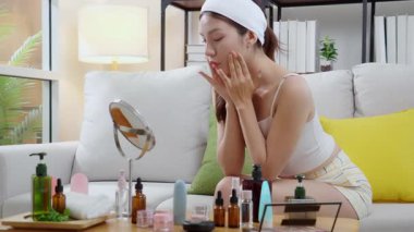 Evdeki oturma odasında kırışıklıkları kontrol etmek için aynaya bakan genç Asyalı güzel bir kadın, nemlendirici süren mutlu bir kadın. Hijyen, cilt bakımı, cilt bakımı, cilt bakımı ve cilt bakımı..