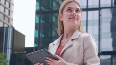 Şehir merkezinde dijital tablet kullanan genç bir iş kadını, kendine güvenen, profesyonel bir iş kadınıyla uzaktan kumandayla çalışıyor. Çevrimiçi ve kurumsal işleri yönetirken gülümsüyor..