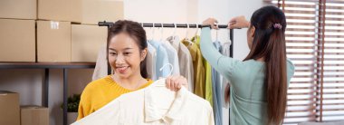 İki genç Asyalı kadın online giyim mağazasında yaşarken, evde sosyal medyada tablet ve dizüstü bilgisayarlı giysiler gösteriliyor. Girişimci çevrimiçi kıyafet satışı ve sunumu için çevrimiçi satış yapıyor..