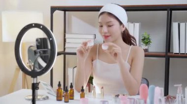 Genç Asyalı kadın kozmetik ürünlerini sosyal medya platformunda takipçiler, krem ya da losyonu canlı yayında inceleyen, etkileyen ve gözden geçiren kadınlar için heyecan verici bir şekilde sunup gözden geçiriyor..