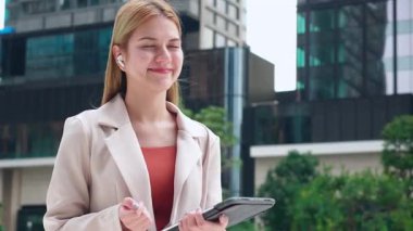 Şehirde dijital tablet tutarken kablosuz kulaklık kullanan profesyonel beyaz iş kadını konuşuyor. İş kadını, iletişim ve kentsel başarı için teknolojiyi kullanıyor..