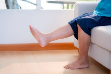 Ayaklarını kapat. Tedavi için bacağını esnet. Oturma odasındaki koltukta diz ağrısı, rutin fizik tedavi diz ve bacak gücü, rehabilitasyon ve kişisel bakım..