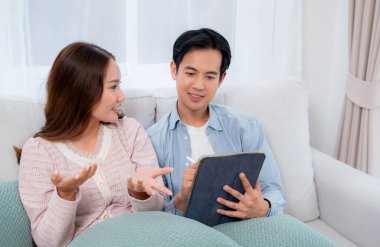 Mutlu Asyalı çift dijital tablet cihazına notlar yazıp planlıyorlar. Oturma odasındaki kanepede oturuyorlar. Genç adam ve kadın online projeleri tartışıyor..