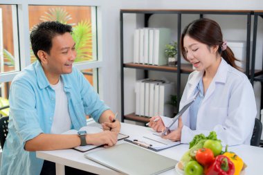 Asyalı beslenme uzmanı, AI ile kişiselleştirilmiş yemek planını sağlık hizmetleri danışmanlığı sırasında hastaya açıklamak için tablet kullanıyor, sağlıklı yaşam tarzı, kadın diyetçisi, tablette yapay zekayla beslenme planı gösteriyor..