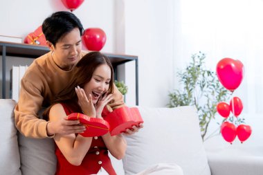 Mutlu Asyalı adam Sevgililer Günü 'nü ya da yıldönümünü evde kutlayan sevgilisine kalp hediye kutusu veriyor. Mutlu sürpriz hediyeye aşık genç bir çift, ilişki ve kaynaşma..