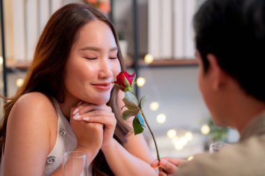 Romantik Asyalı bir adam yemek sırasında gülümseyen bir kadına gül veriyor, Sevgililer Günü ya da yıldönümü kutlaması için sürpriz bir hediye, restoranda birbirine aşık bir çift, birbirini seven ve kaynaşan bir çift..