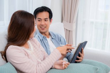 Mutlu Asyalı çift dijital tablet cihazına notlar yazıp planlıyorlar. Oturma odasındaki kanepede oturuyorlar. Genç adam ve kadın online projeleri tartışıyor..