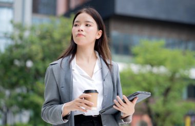 Tablet kullanırken elinde kahve tutan Asyalı genç iş kadını, dijital göçebe, iş kadını ya da yönetici tablete dokunuyor, modern teknoloji, dijital cihaz..