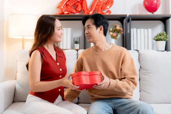 Mutlu Asyalı adam Sevgililer Günü 'nü ya da yıldönümünü evde kutlayan sevgilisine kalp hediye kutusu veriyor. Mutlu sürpriz hediyeye aşık genç bir çift, ilişki ve kaynaşma..