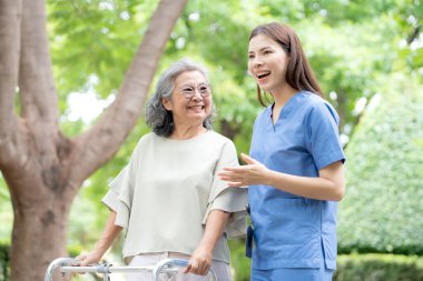Asyalı kadın bakıcı, Walker 'a fiziksel rehabilitasyon ve terapi için yardım ediyor. Hemşire, parkta yürüyen yaşlı kadına bakıyor. Sağlık ve sağlıklı emeklilik..
