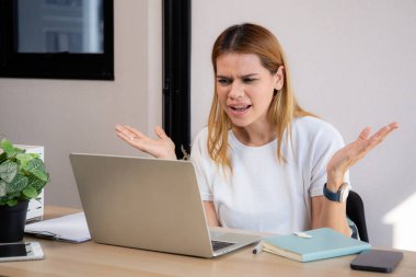 Mutsuz Kafkasyalı genç iş kadını masadaki dizüstü bilgisayarını kullanıyor. Ofiste stresli ve bitkin durumda. İş kadını hayal kırıklığına uğramış ve kaygılı bir şekilde dizüstü bilgisayarda çalışıyor..