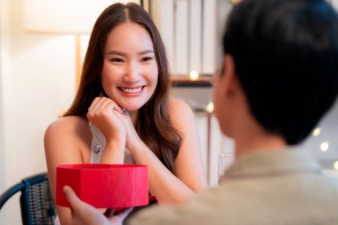 Romantik Asyalı adam sevgilisine kalp şeklinde hediye kutusu veriyor sevgililer günü sürprizi ya da restoranda yıldönümü yemeği mutlu çifti hediyeyle, mutlulukla ve ilişkiyle kutluyor..