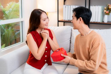 Mutlu Asyalı adam Sevgililer Günü 'nü ya da yıldönümünü evde kutlayan sevgilisine kalp hediye kutusu veriyor. Mutlu sürpriz hediyeye aşık genç bir çift, ilişki ve kaynaşma..