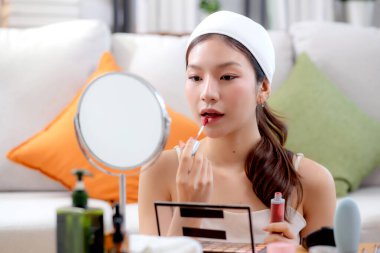 Güzel, mutlu, Asyalı bir kadın. Oturma odasında aynaya ruj sürerek makyaj yapıyor. Güzel bir kadın makyaj yapıyor..