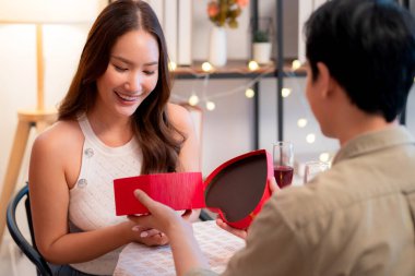 Romantik Asyalı adam sevgilisine kalp şeklinde hediye kutusu veriyor sevgililer günü sürprizi ya da restoranda yıldönümü yemeği mutlu çifti hediyeyle, mutlulukla ve ilişkiyle kutluyor..