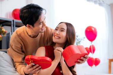 Mutlu Asyalı adam Sevgililer Günü 'nü ya da yıldönümünü evde kutlayan sevgilisine kalp hediye kutusu veriyor. Mutlu sürpriz hediyeye aşık genç bir çift, ilişki ve kaynaşma..