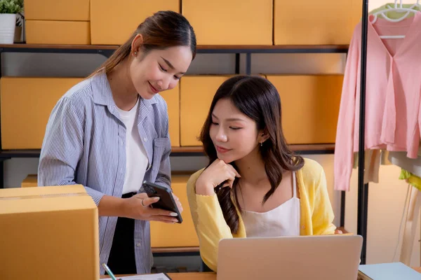 Küçük işletme online mağazasında çalışan iki Asyalı kadın, çevrimiçi satıcı, girişimci iş kadını takım akıllı telefon ve dizüstü bilgisayarla envanter siparişini kontrol ediyor..