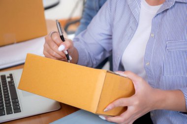 Kapalı el Asyalı genç kadın paket kutusuna adres yazıyor. Müşteri, nakliyat ve lojistik, tüccar ve satıcı, girişimci ya da KME, çevrimiçi alışveriş için..