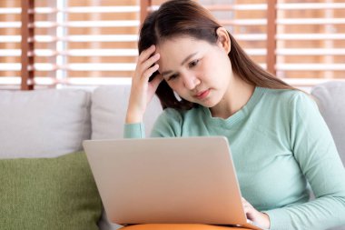 Genç Asyalı iş kadını evde stresli ve hayal kırıklığına uğramış bir şekilde dizüstü bilgisayarla çalışıyor, iş kadını defterinde üzgün ve yorgun olarak kullanıyor, ifade ve duygu, iş ve yaşam tarzı.