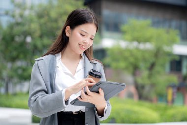 Tablet kullanırken elinde kahve tutan Asyalı genç iş kadını, dijital göçebe, iş kadını ya da yönetici tablete dokunuyor, modern teknoloji, dijital cihaz..