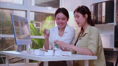 Kozmetik ambalaj tasarımı geliştirme için yapay zeka asistanı kullanan iki Asyalı kadın tasarımcı, yaratıcı takım işi pazarlama, fikir için yapay zeka ile ürün tasarımı projesi.