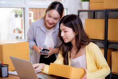 Küçük işletme online mağazasında çalışan iki Asyalı kadın, çevrimiçi satıcı, girişimci iş kadını takım akıllı telefon ve dizüstü bilgisayarla envanter siparişini kontrol ediyor..