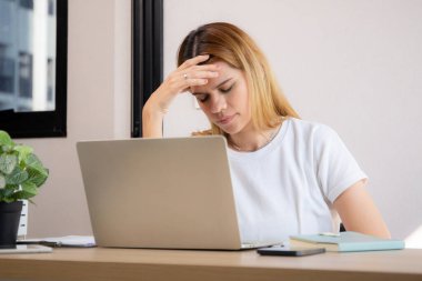 Mutsuz Kafkasyalı genç iş kadını masadaki dizüstü bilgisayarını kullanıyor. Ofiste stresli ve bitkin durumda. İş kadını hayal kırıklığına uğramış ve kaygılı bir şekilde dizüstü bilgisayarda çalışıyor..