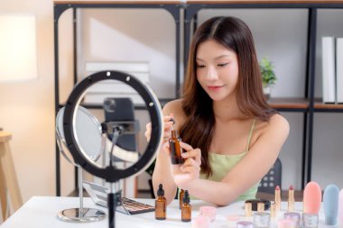 Güzellik değerlendirmesi için sosyal medyada serum, cilt bakımı ve kozmetik içeriği sergileyen Asyalı genç bir kadın güzellik ürünleri ve canlı yayın, yaşam tarzı ve cilt bakımı.