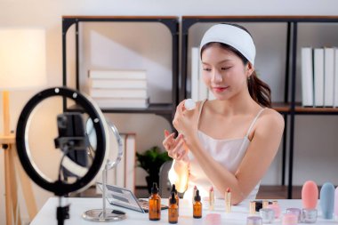 Sosyal medyada kozmetik ürünü sunan ve gözden geçiren Asyalı genç bir kadın, cilt kremi ürünlerini telefonla, canlı yayında ya da yayında inceleyen güzellik uzmanı, içerik yaratıcısı.