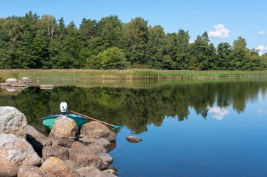 Motorlu ve kürekli tekne bir orman gölünün kıyısına demirlemiş..